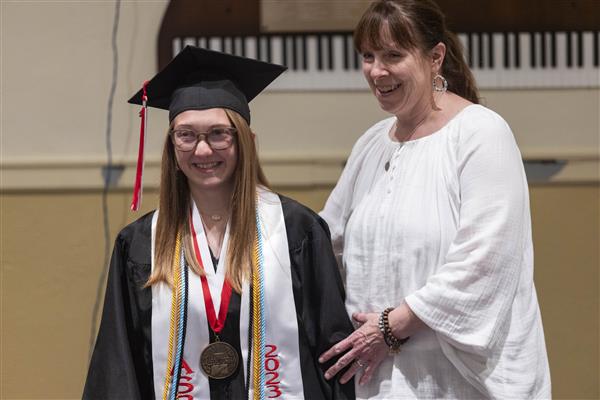 A graduate walks down the aisle towards their seat.